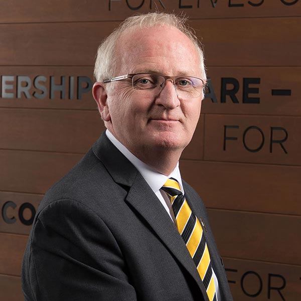 PLU President, Allan Belton, standing in an office with words on the wall behind him