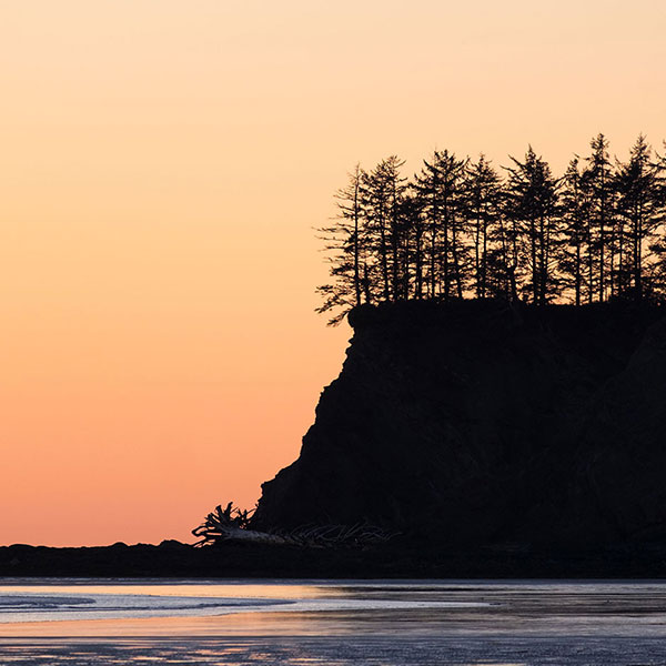 A beautiful orange sunset with soft waves crashing onto the beach in Neah Bay