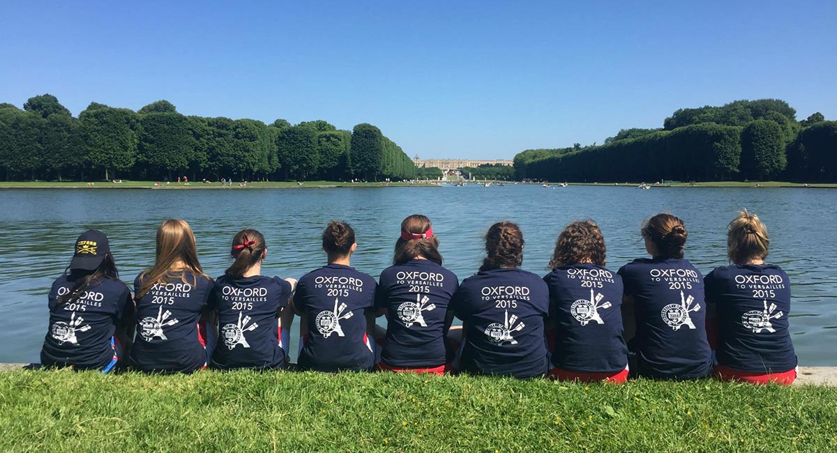 The Oxford women's crew team sitting by lake wearing their "Oxford to Versailles 2015" shirts