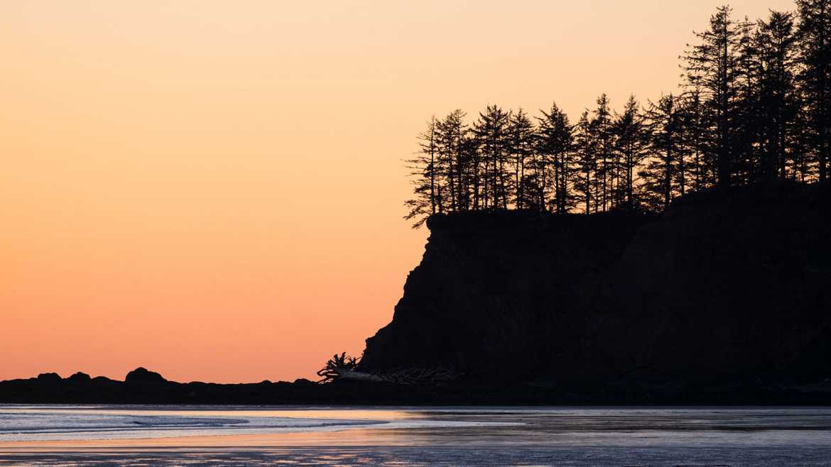 A beautiful orange sunset with soft waves crashing onto the beach in Neah Bay