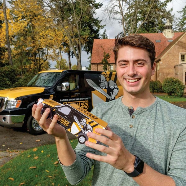 Colton Walter ’19 holds a mockup of a PLU-themed van. He crafted the black-and-gold design for the vehicle.