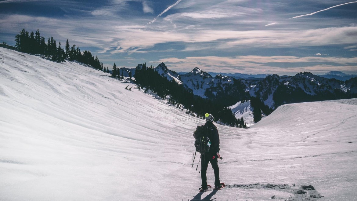 A man is standing on a snow hill up in the mountains