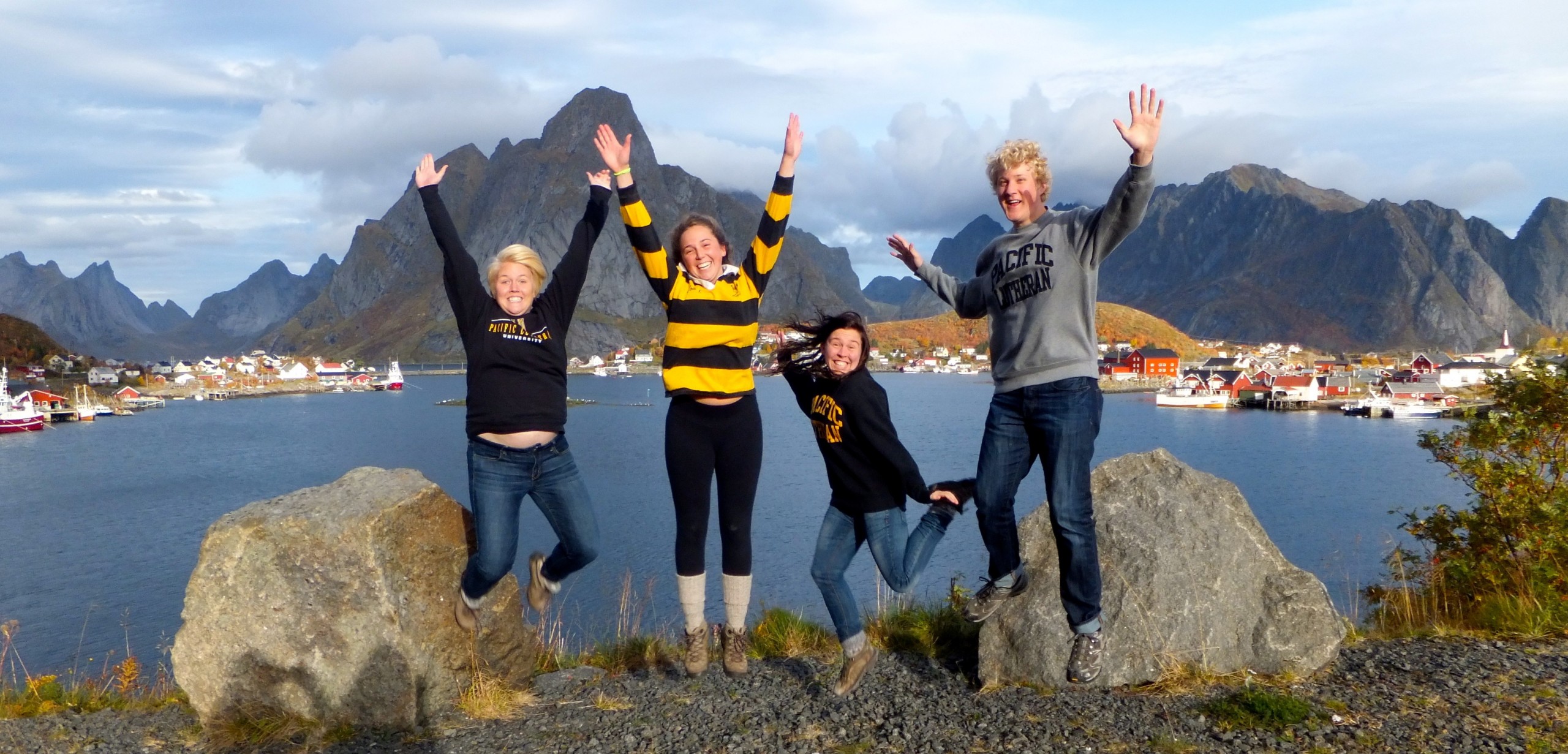 Students jumping up in front of town on water