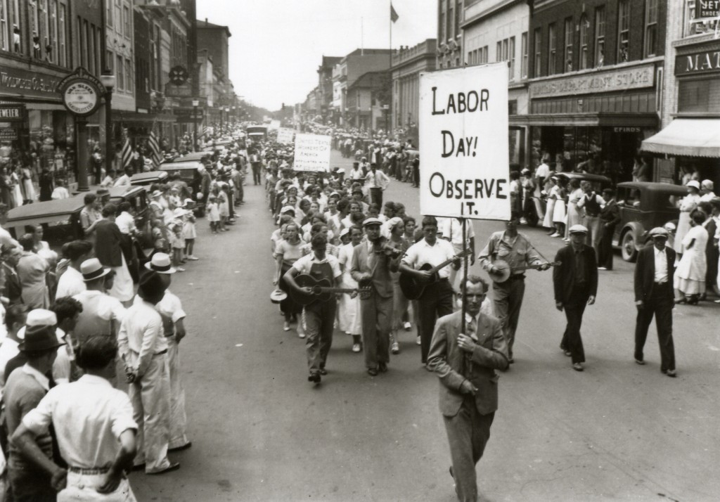 01_uprising-1024x714 Old black & white photo of people walking down the road with a sign that says Labor Day! Observe It.