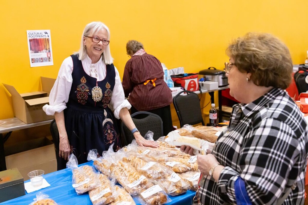 20250315_SB_Norwegian-Heritage-Fest_030-medium Janet Ruud wearing bunad, greeting someone over table selling pastry