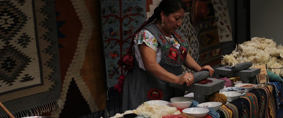 Woman from Oaxaca crushing cochineal bugs using traditional methods, surrounded by natural dyed fibers