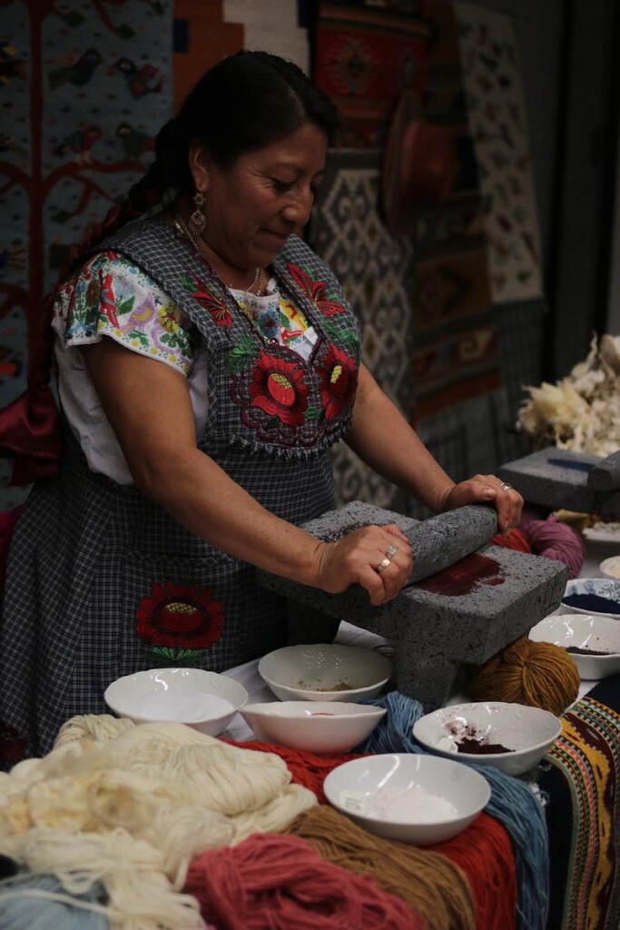 Woman crushing cochineal bugs with traditional stone tools to make red dye