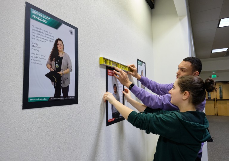 A poster exhibition designed and installed by Native American & Indigenous Studies students Fall 2019 - students putting their posters on the wall