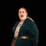 Woman performing on stage in green jacket and theatrical costume