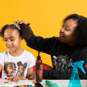 A mother brushes her daughter's hair with a yellow background