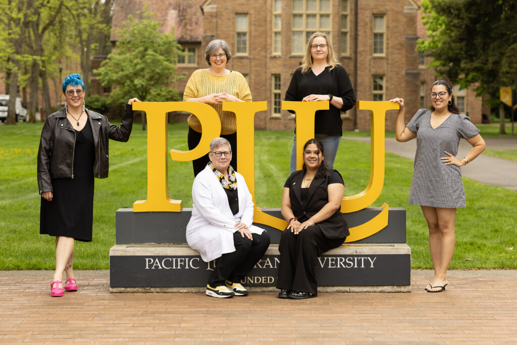 Image of CSS staff members standing around and sitting on the large gold PLU sign at the front of the PLU campus.