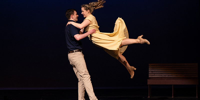 A woman in a yellow dress is swung around by a male partner with her ponytail streaming behind her.