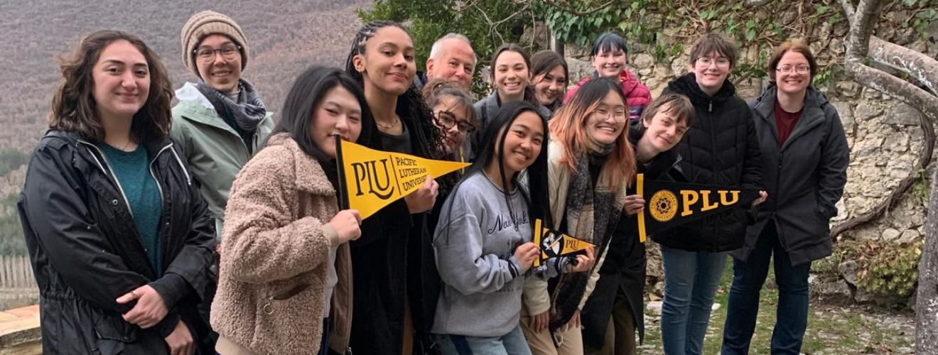 A group of students stands in front of a rocky wall holding PLU penants