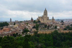2017 Spain and Portugal University Wind Ensemble Trip - A large cityscape featuring numerous buildings, with the historic Segovia castle visible in the background against a partially cloudy sky.